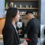 Modernus kavos aparatas šviesiame biure ant stalo šalia šviežios kavos puodelio.